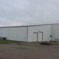 White industrial building with two loading doors under a cloudy sky.