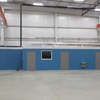 Blue wall with doors, small window, and grey floor in a large, bright industrial space.