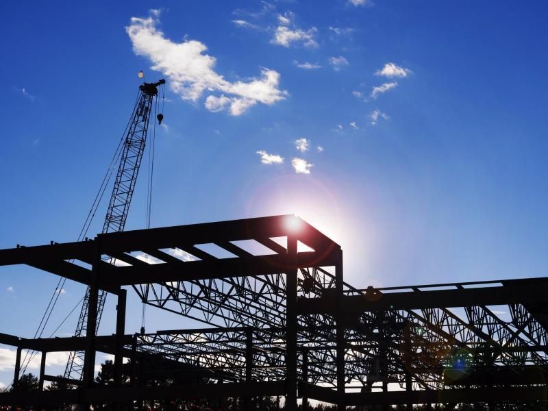 Silhouette of a steel construction frame and crane against a bright, sunny blue sky.