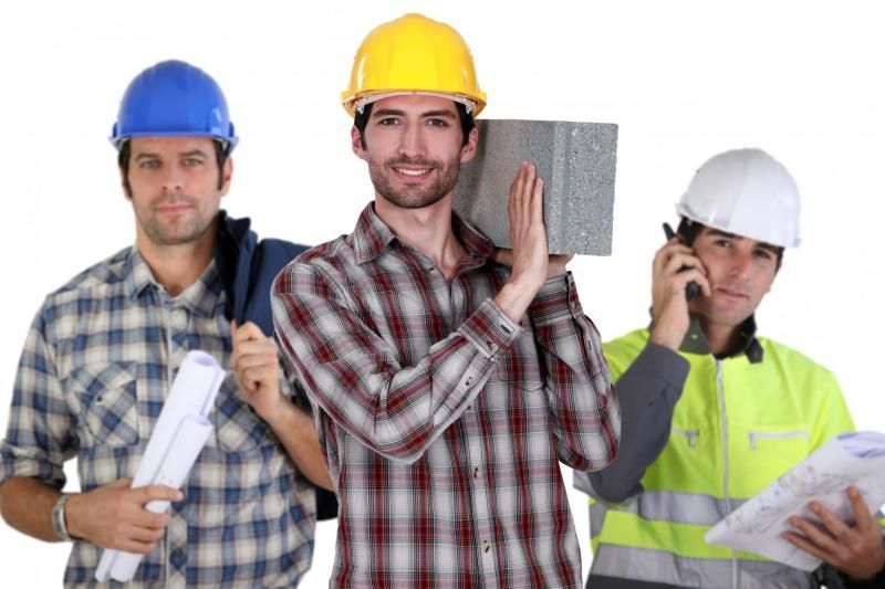 Three construction workers in hard hats, one carrying a block, one with blueprints, and one on a phone.