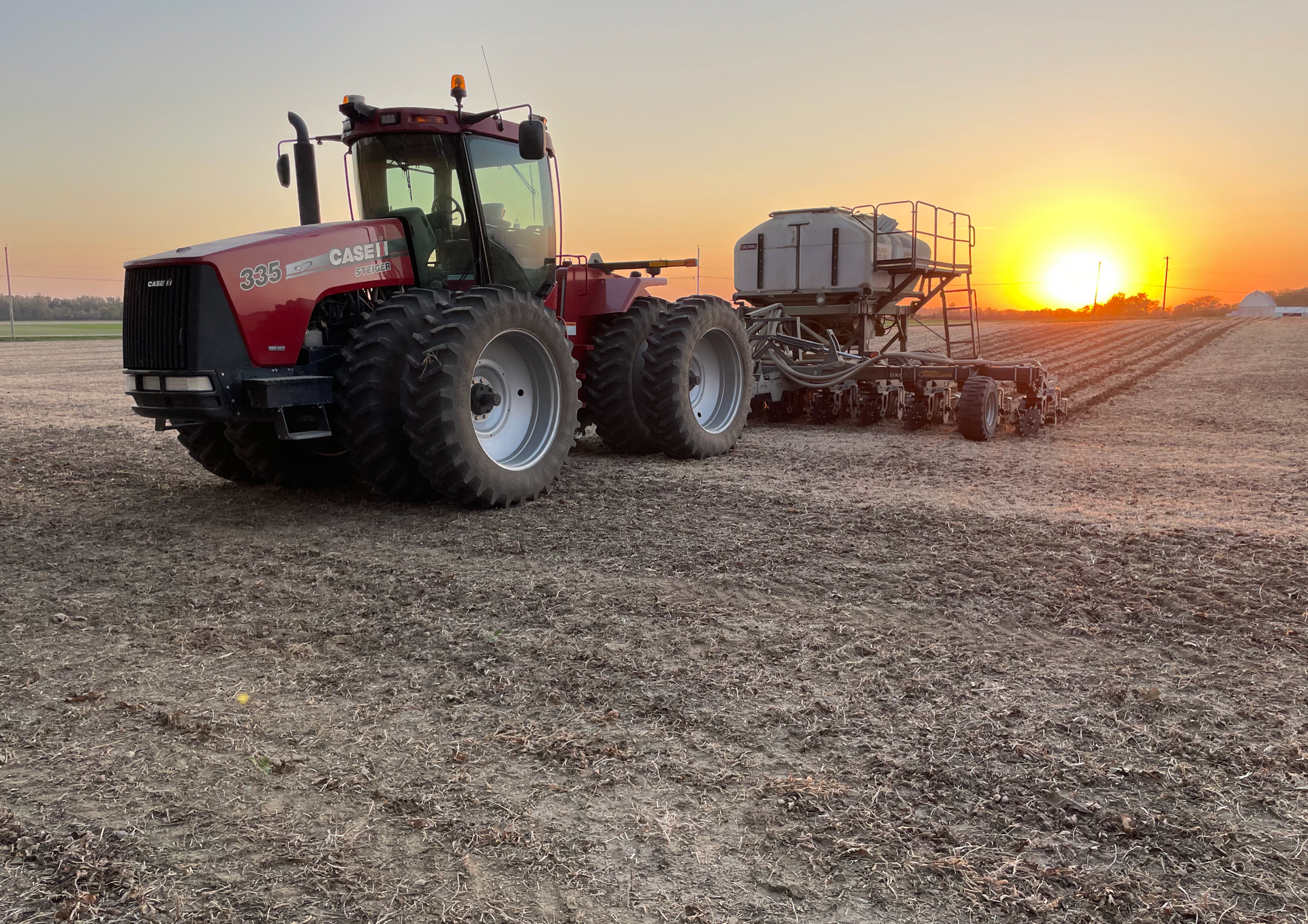 Red tractor pulling a seeder across a field at sunset.