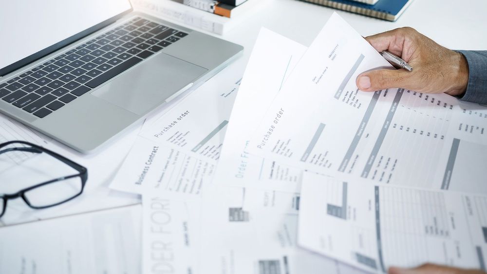 A person is holding a piece of paper in front of a laptop computer.