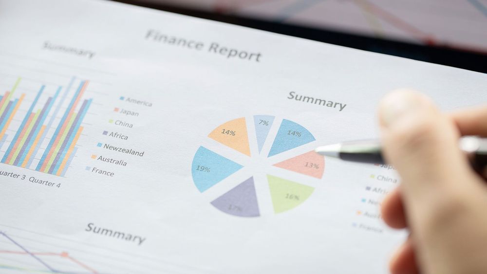 A person is pointing at a pie chart on a finance report.