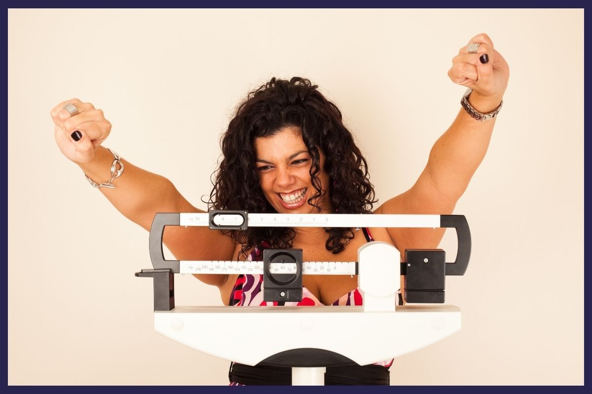 A woman stands on a scale with her arms raised, representing health at a premier personalized medical care clinic.
