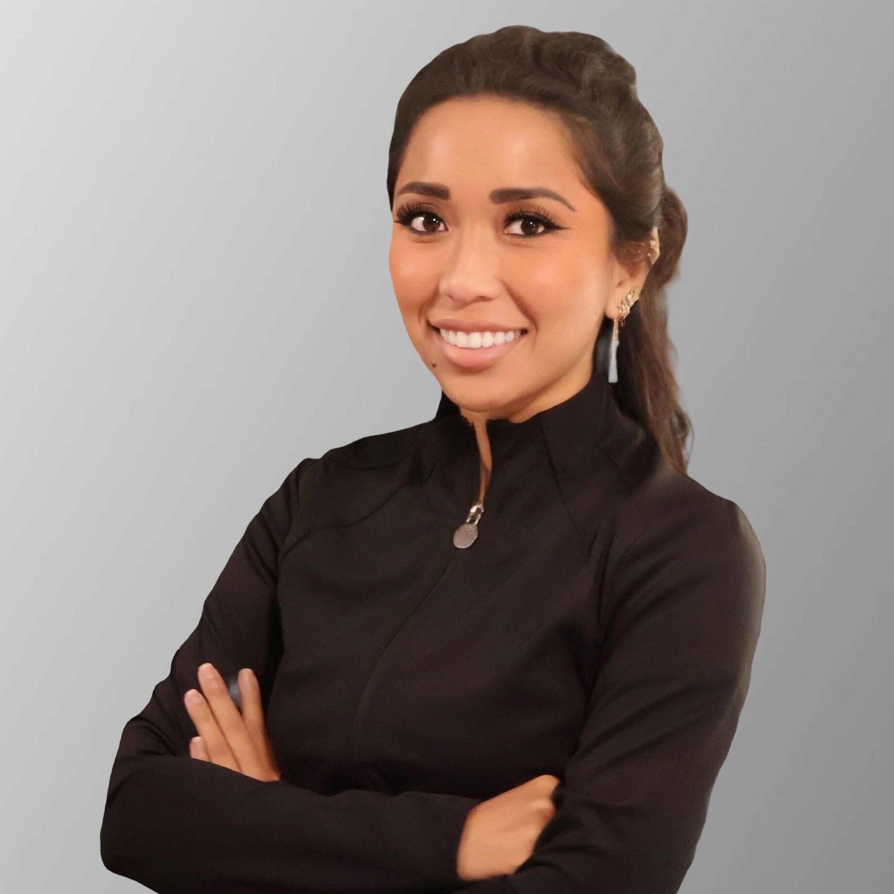 Woman with short blonde hair smiles in a white coat, outdoors in front of a building.