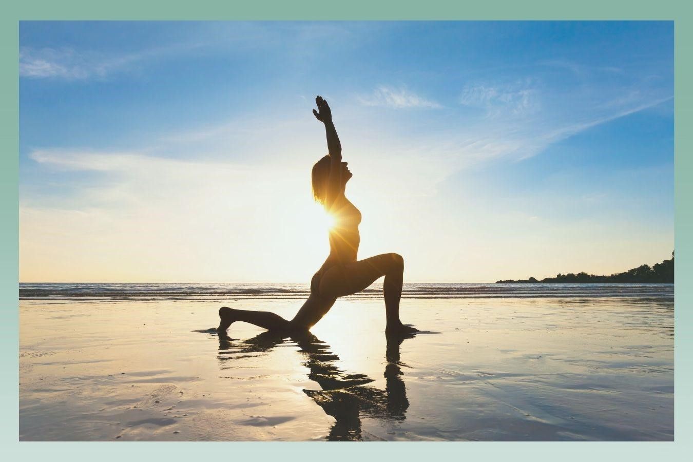 Silhouette of a person doing a yoga pose on a beach at sunset; arms raised to the sky.