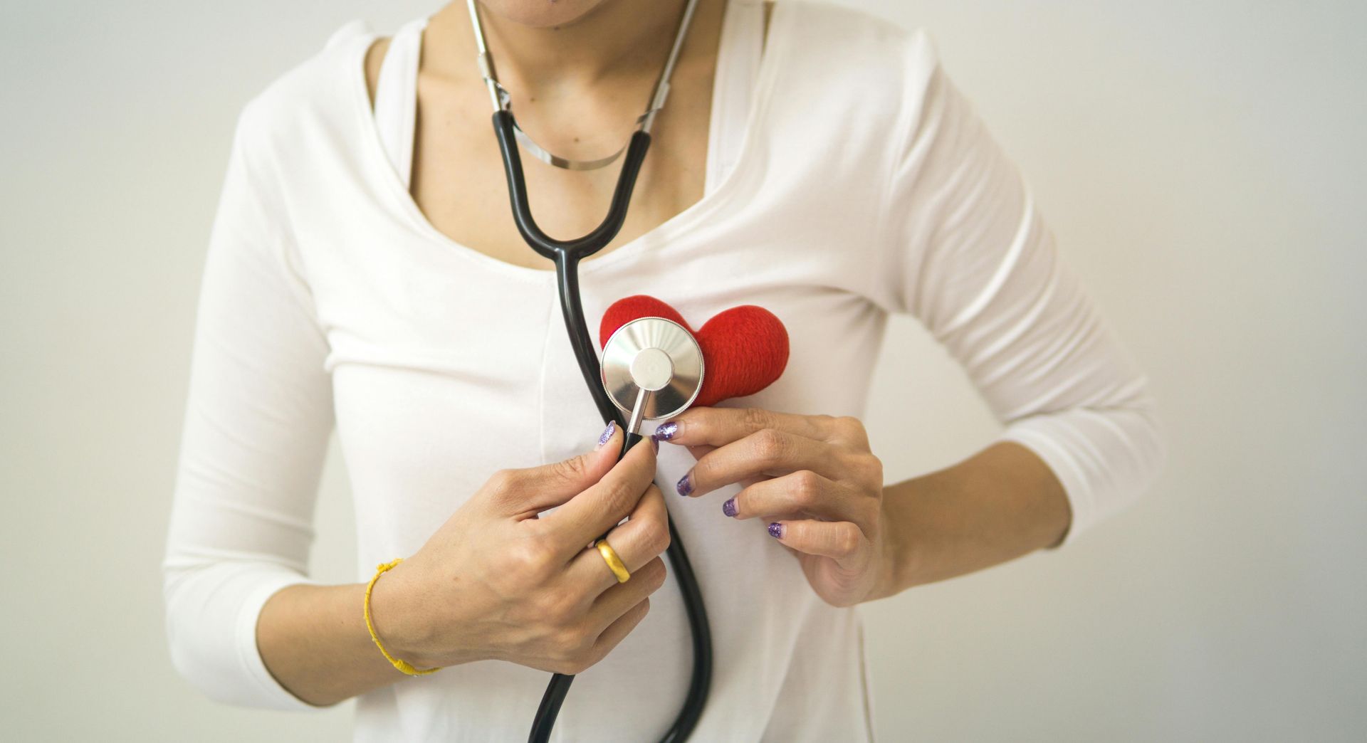 Woman with stethoscope listens to red heart on chest.