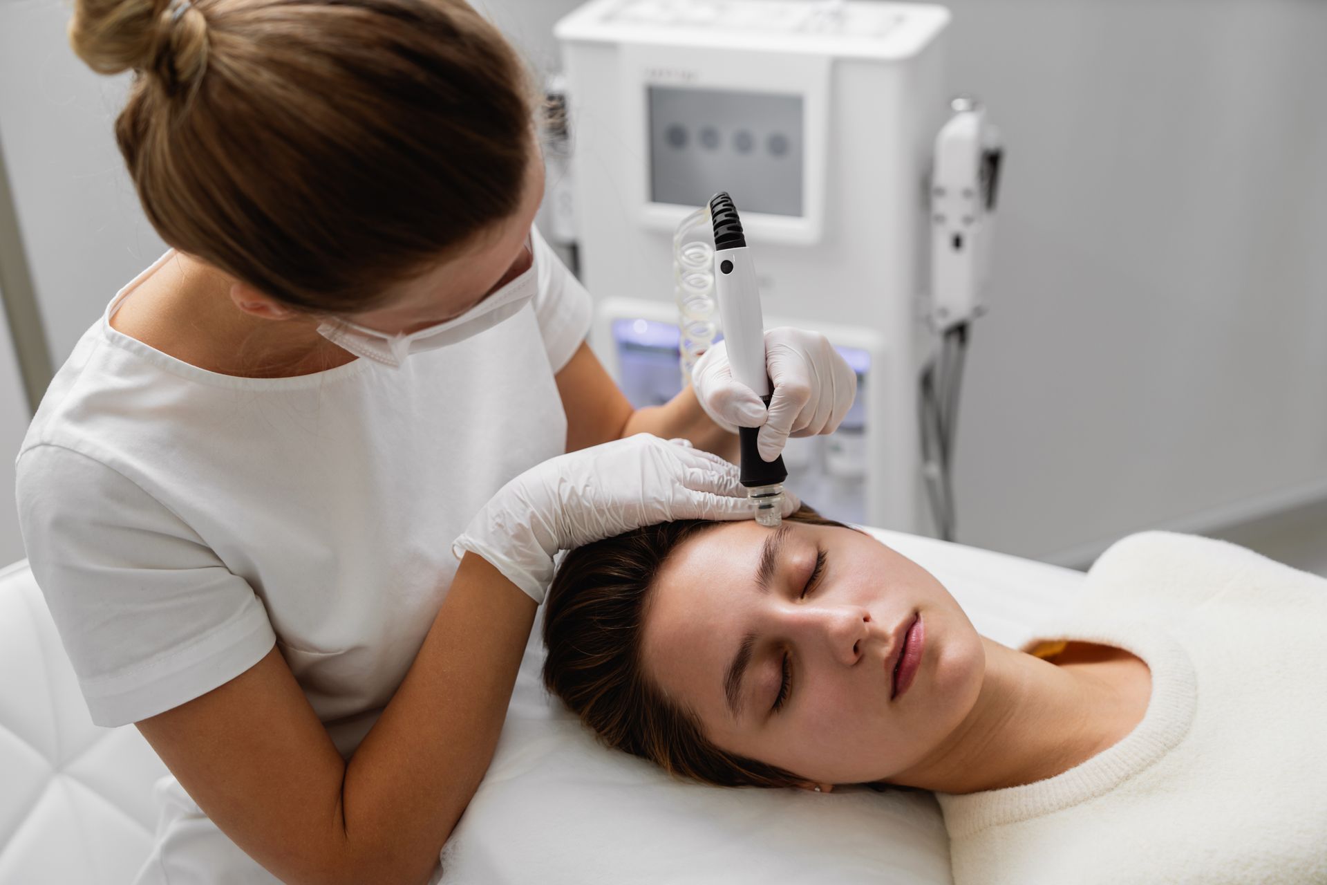 Woman receiving facial treatment from a technician in a medical setting.