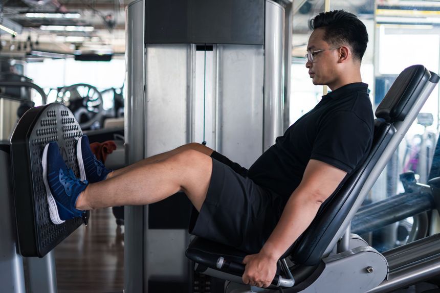 Man in black shirt doing leg press exercise at a gym.
