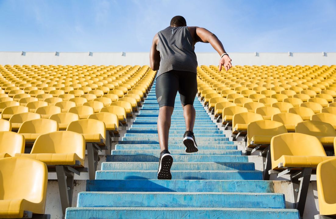 Man running up stadium steps, wearing athletic wear, with yellow seats in background.