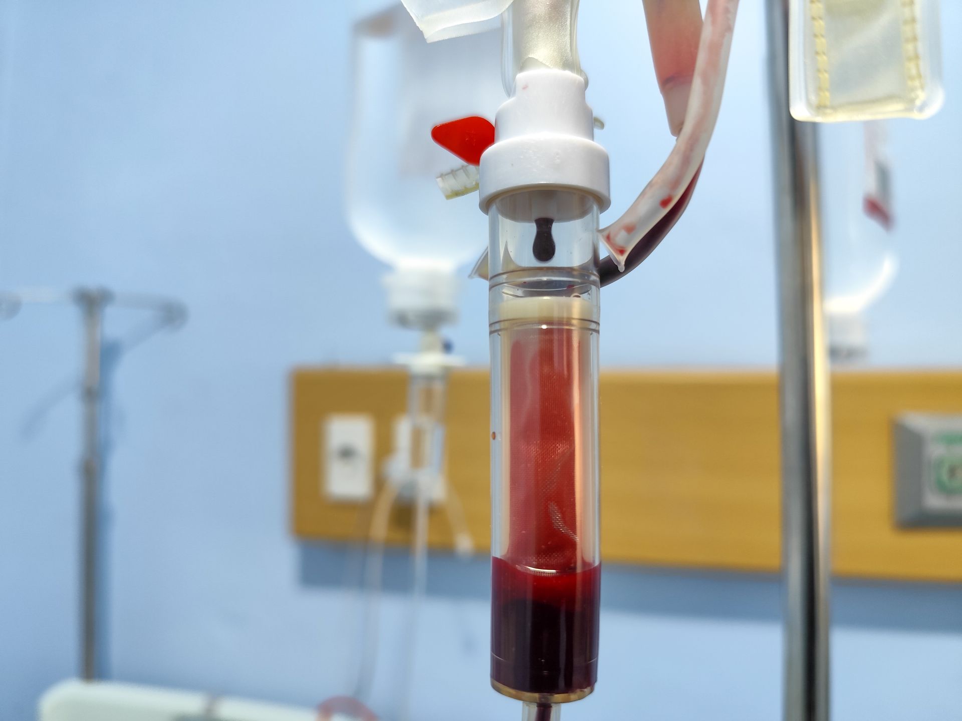 Blood transfusion setup with a red fluid dripping into a clear chamber, in a hospital room.