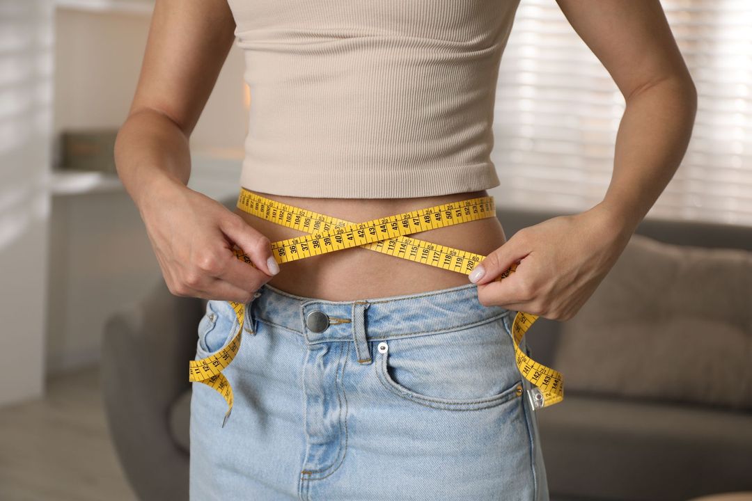 Woman measuring waist with yellow tape in a light-filled room.