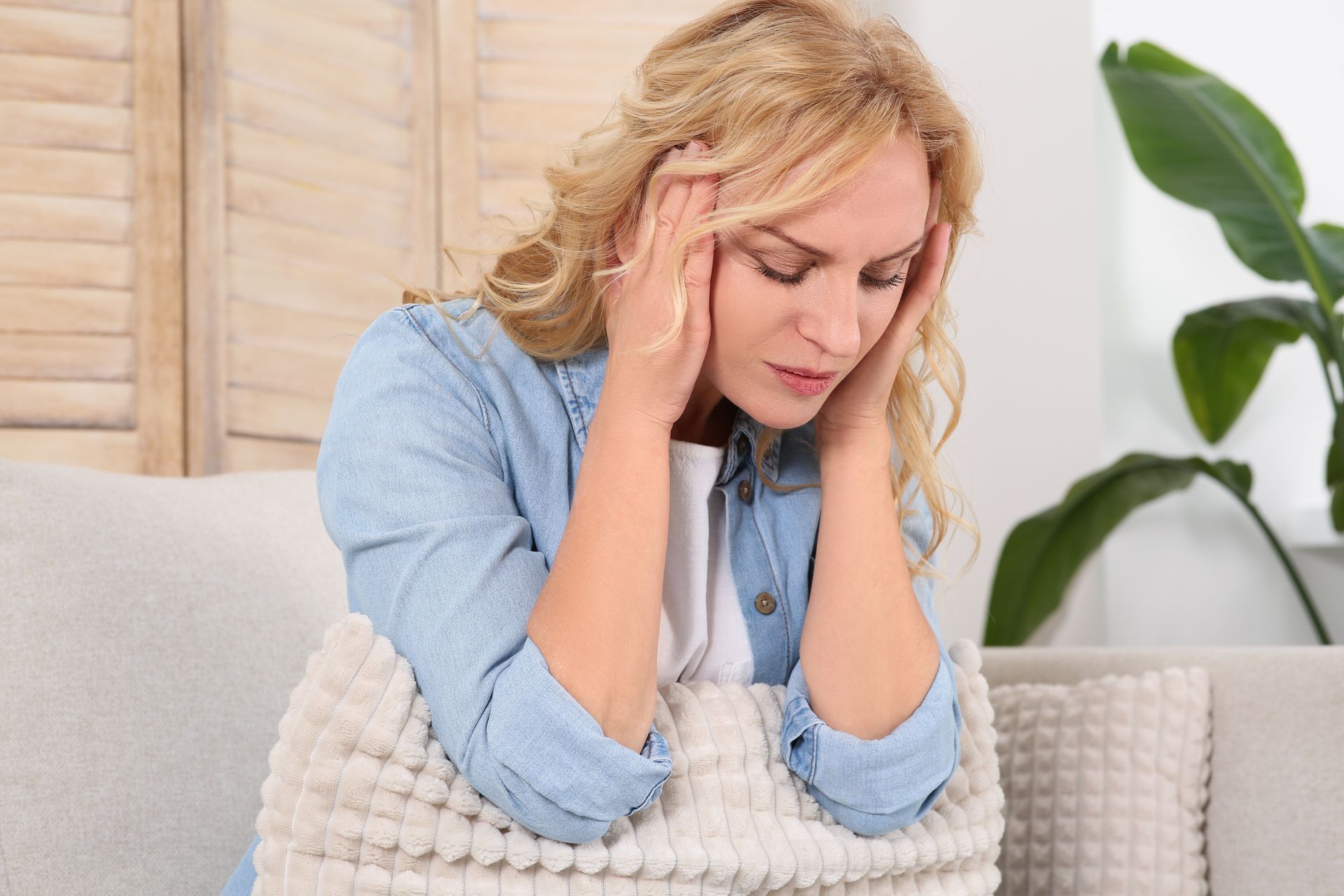 Woman with blonde hair, holding head in hands, looking distressed.