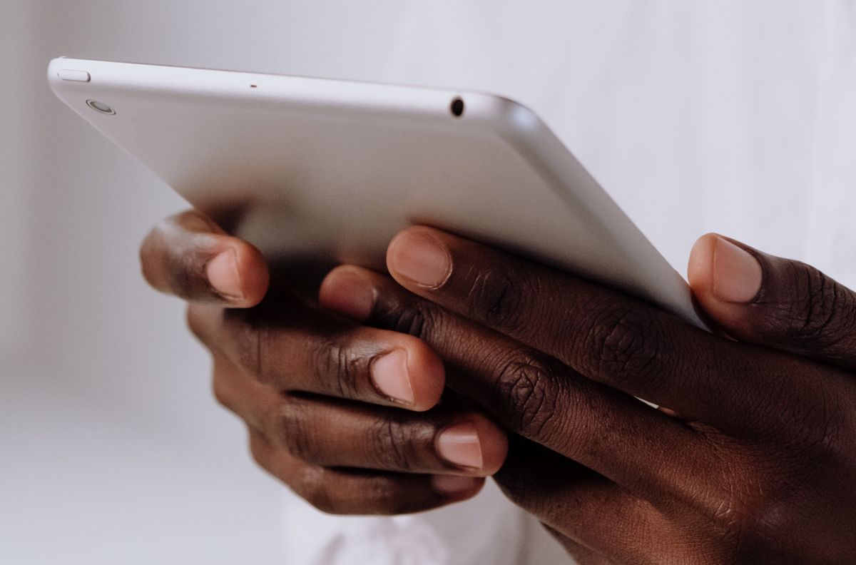 Dark-skinned hands hold a silver tablet.