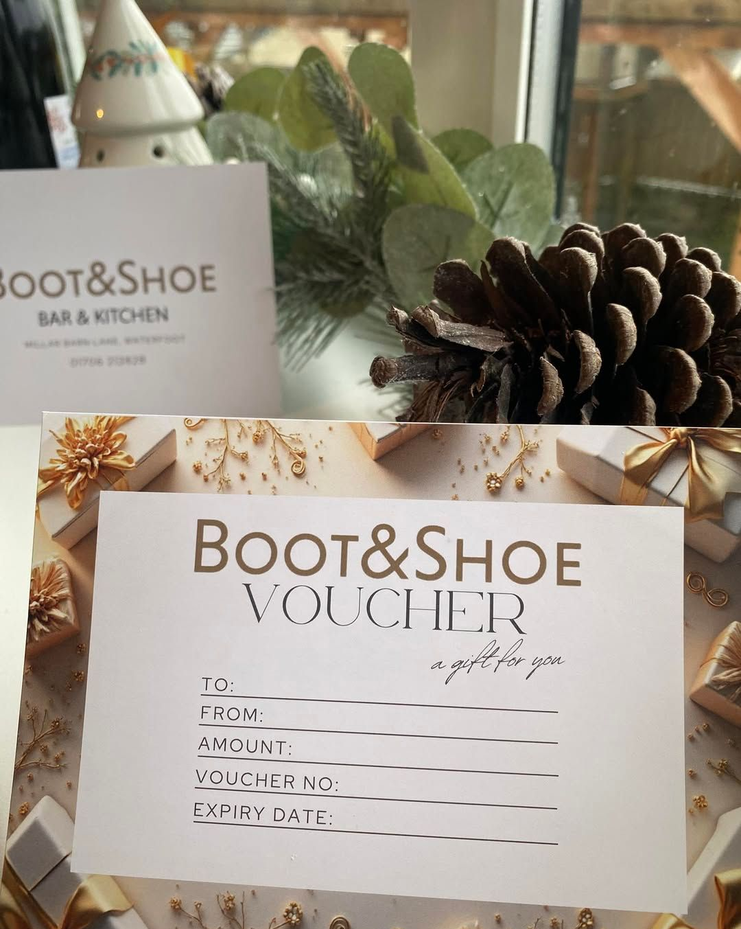 Boot & Shoe gift voucher, white and gold design, for a bar and kitchen, with decorative pine cone and sprigs.