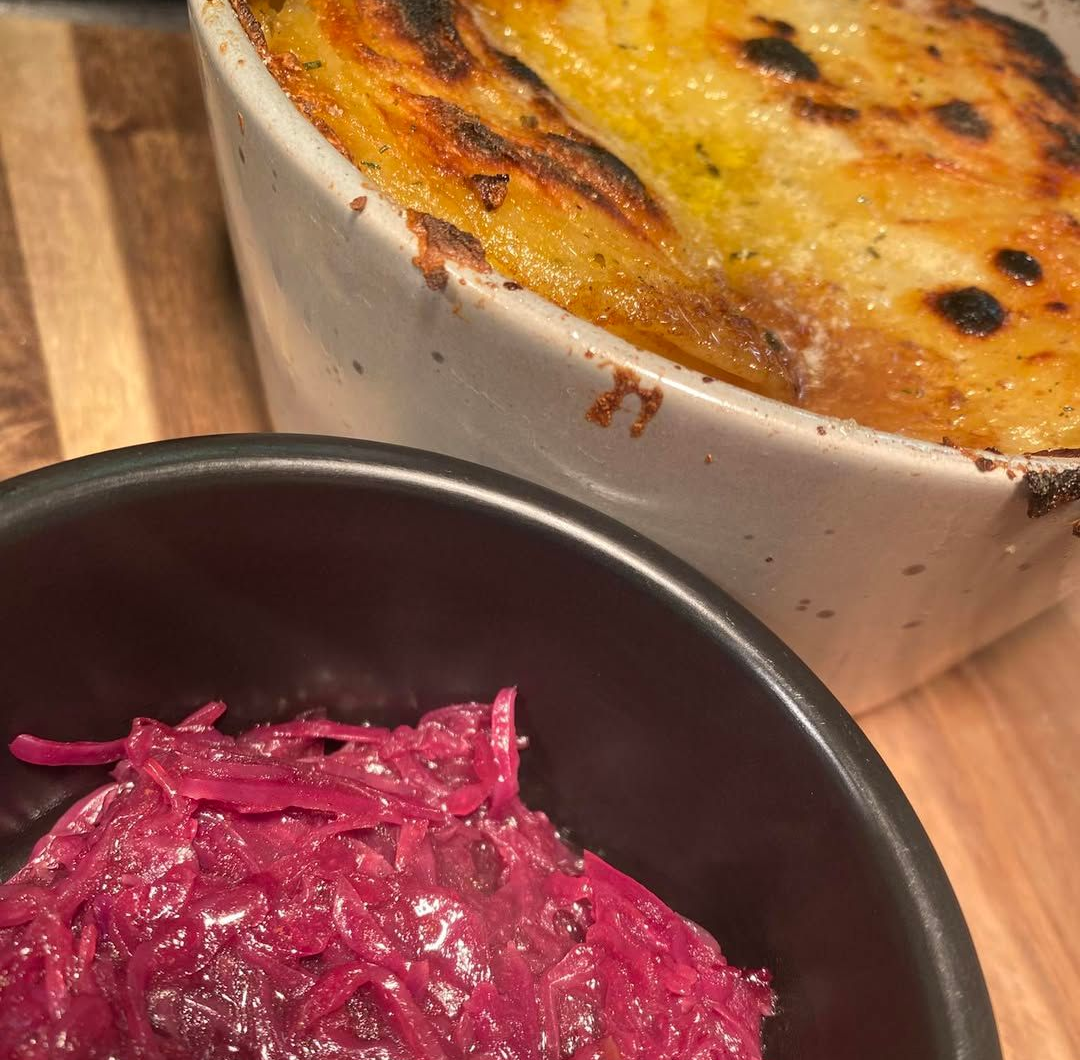 Baked dish with golden crust next to a bowl of red cabbage. On a wooden surface.