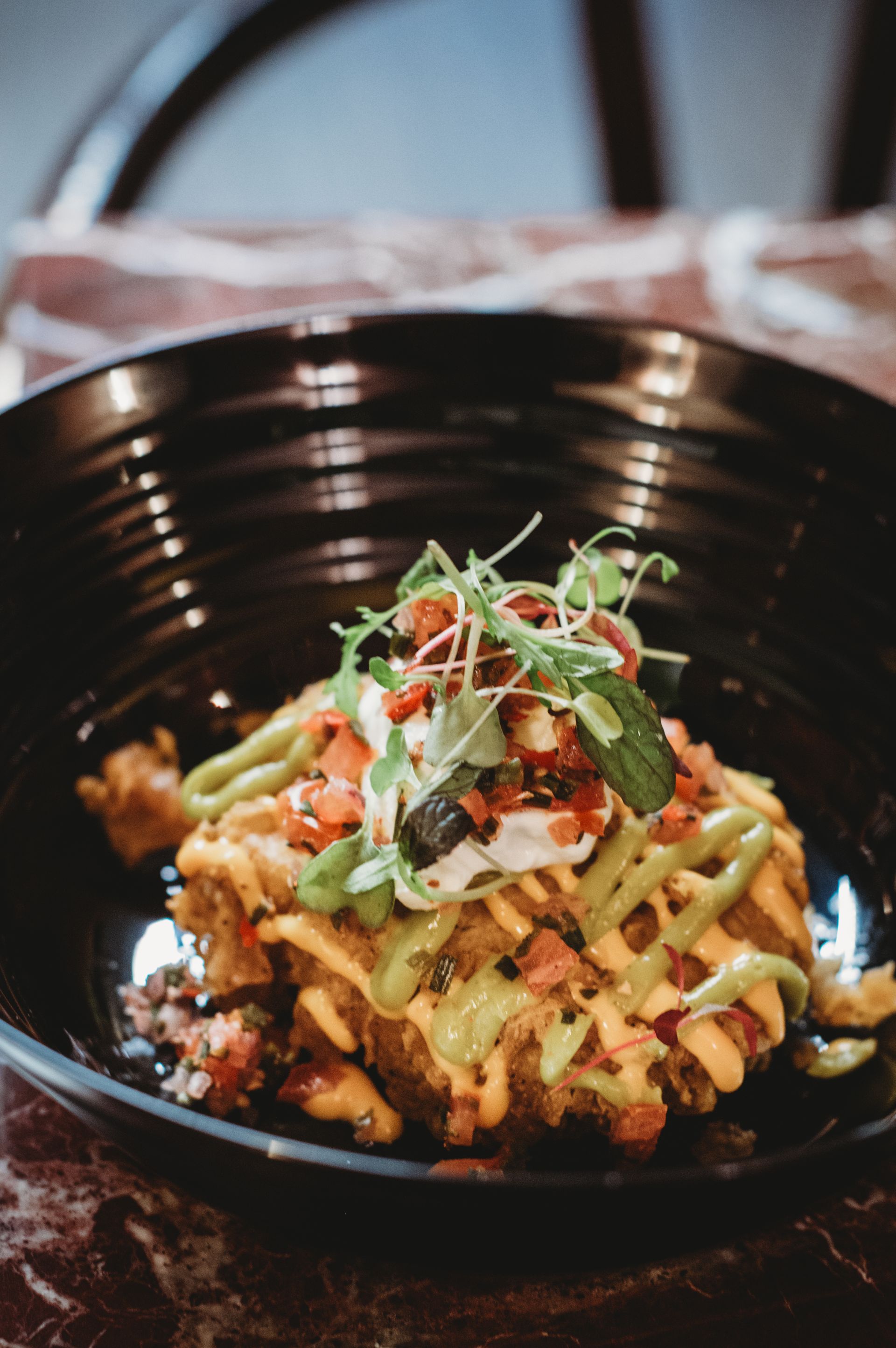 Dish of food with green and orange sauces, white cream, and garnish in a black bowl.