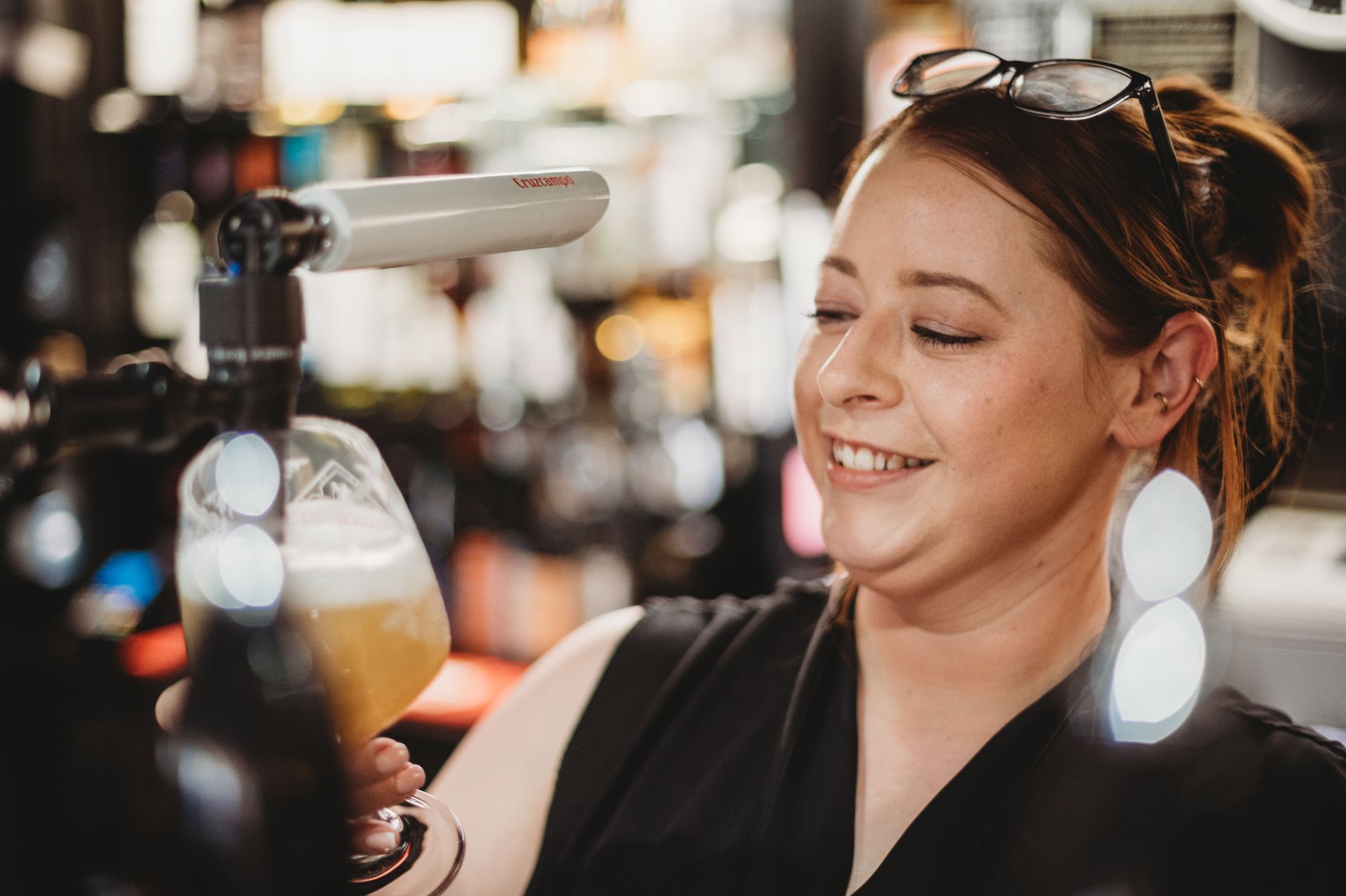 Bartender pouring beer from a tap into a glass, smiling. Pub setting.