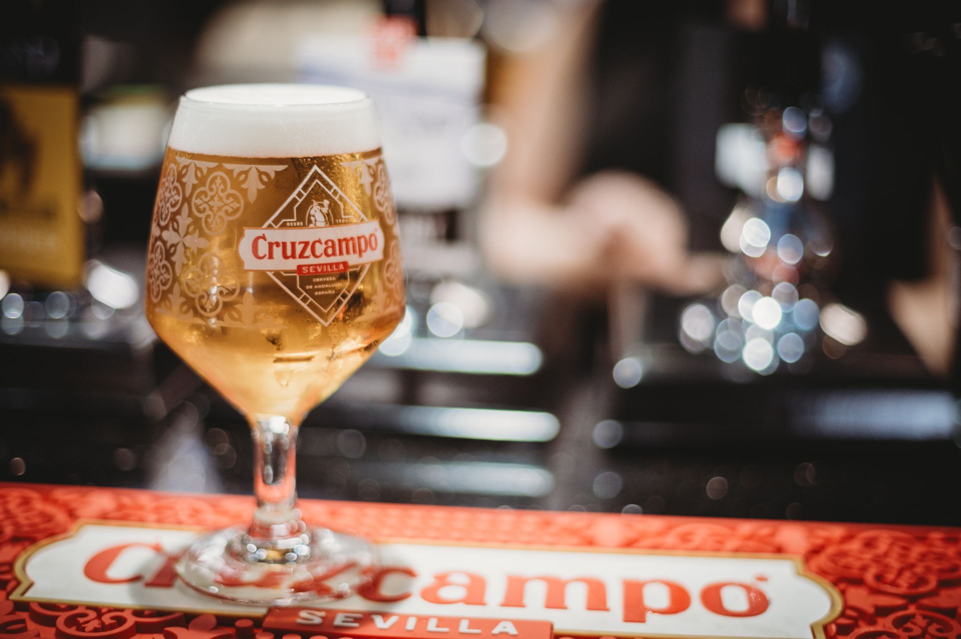 Glass of Cruzcampo beer on a bar, with a red sign featuring the brand logo. at the Boot & Shoe Waterfoot, Rossendale