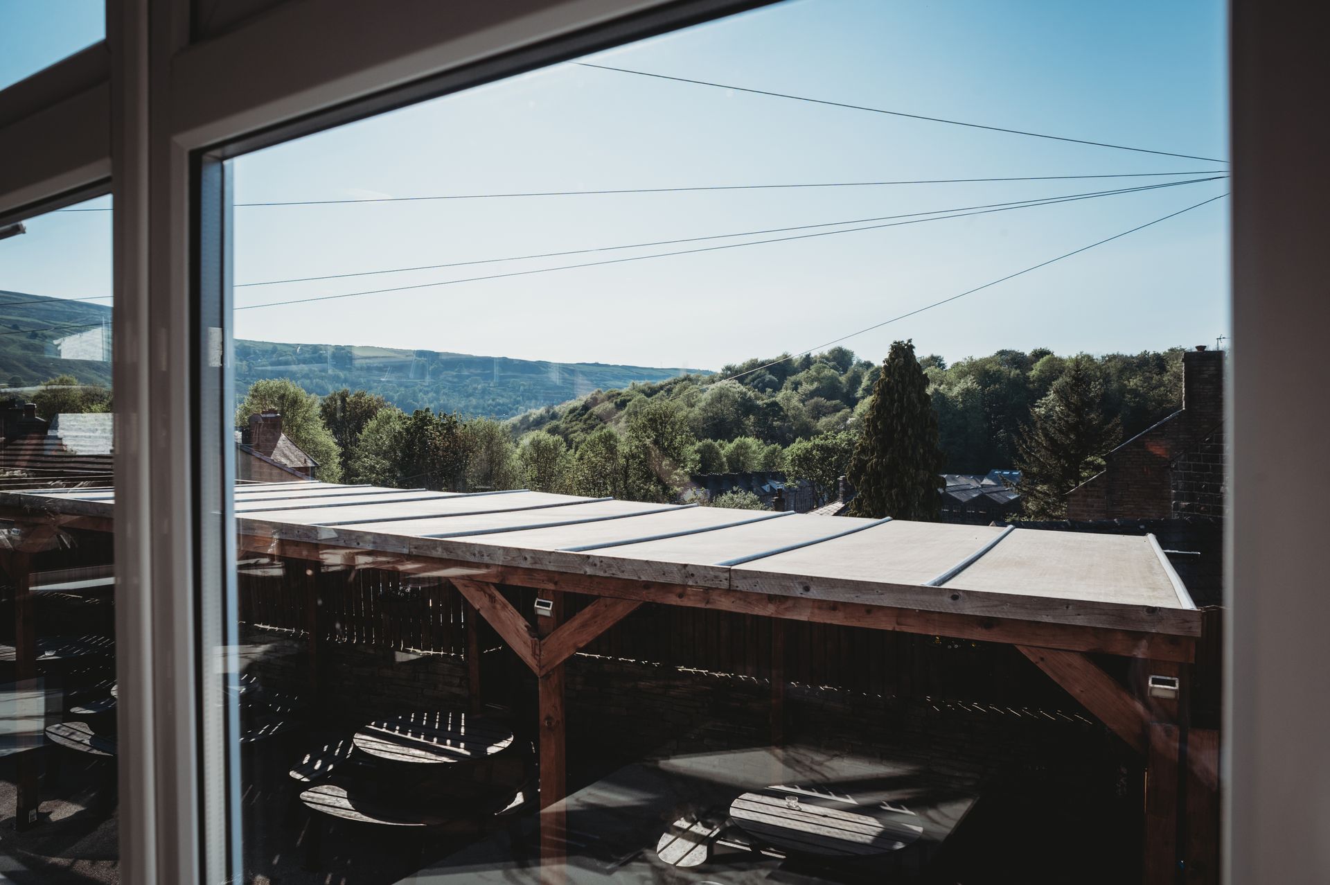 View of trees and hills from a window, with a covered patio below. Blue sky overhead.