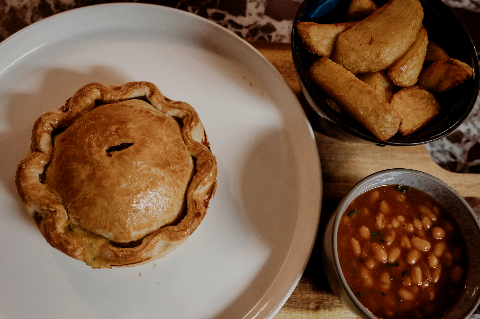 Meat pie with gravy, green beans, and a side of mashed potato on a plate. Gravy being poured on top.