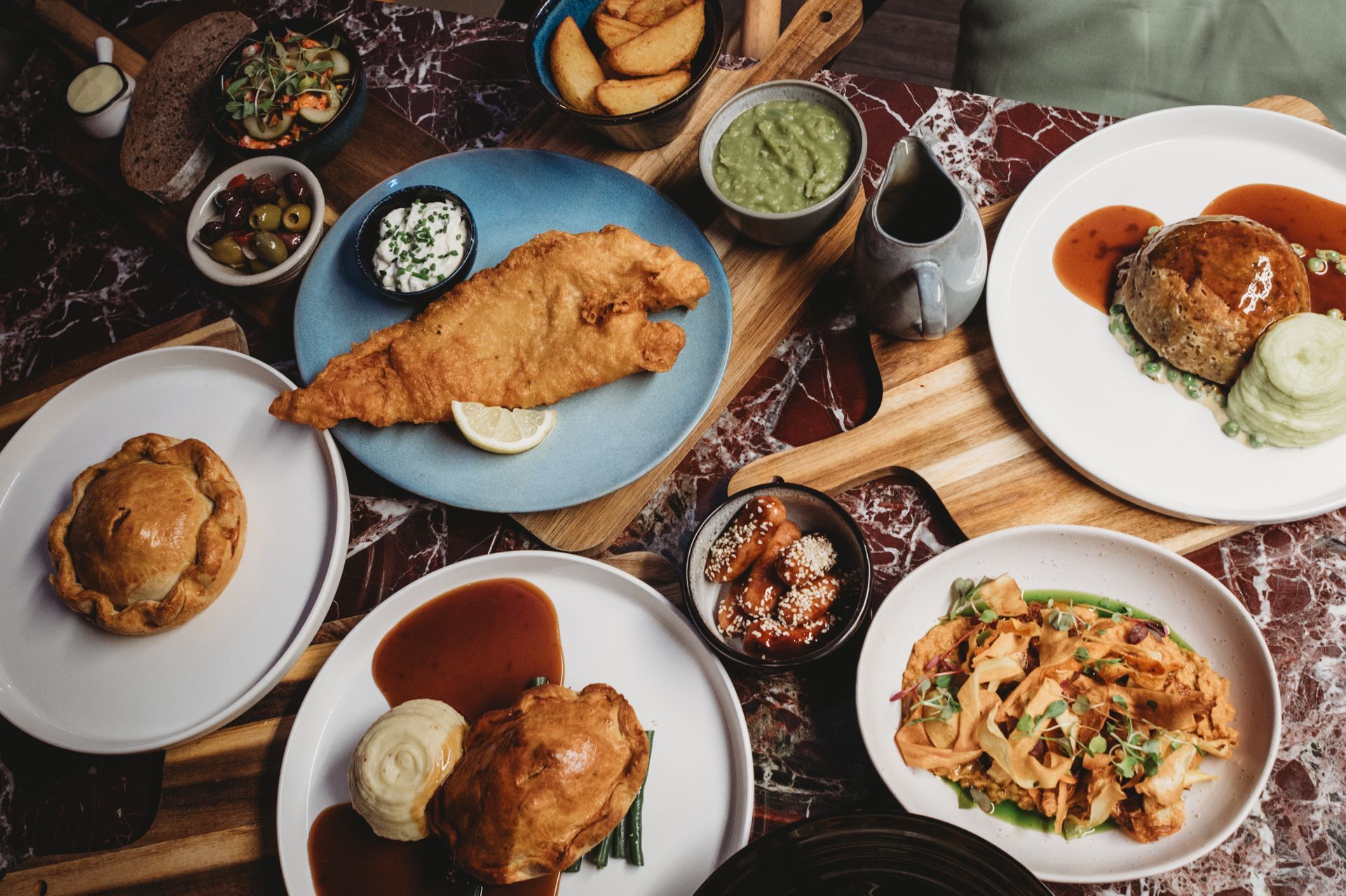 Overhead view of a table with various dishes: fish, pies, potatoes, salad, and sauces.