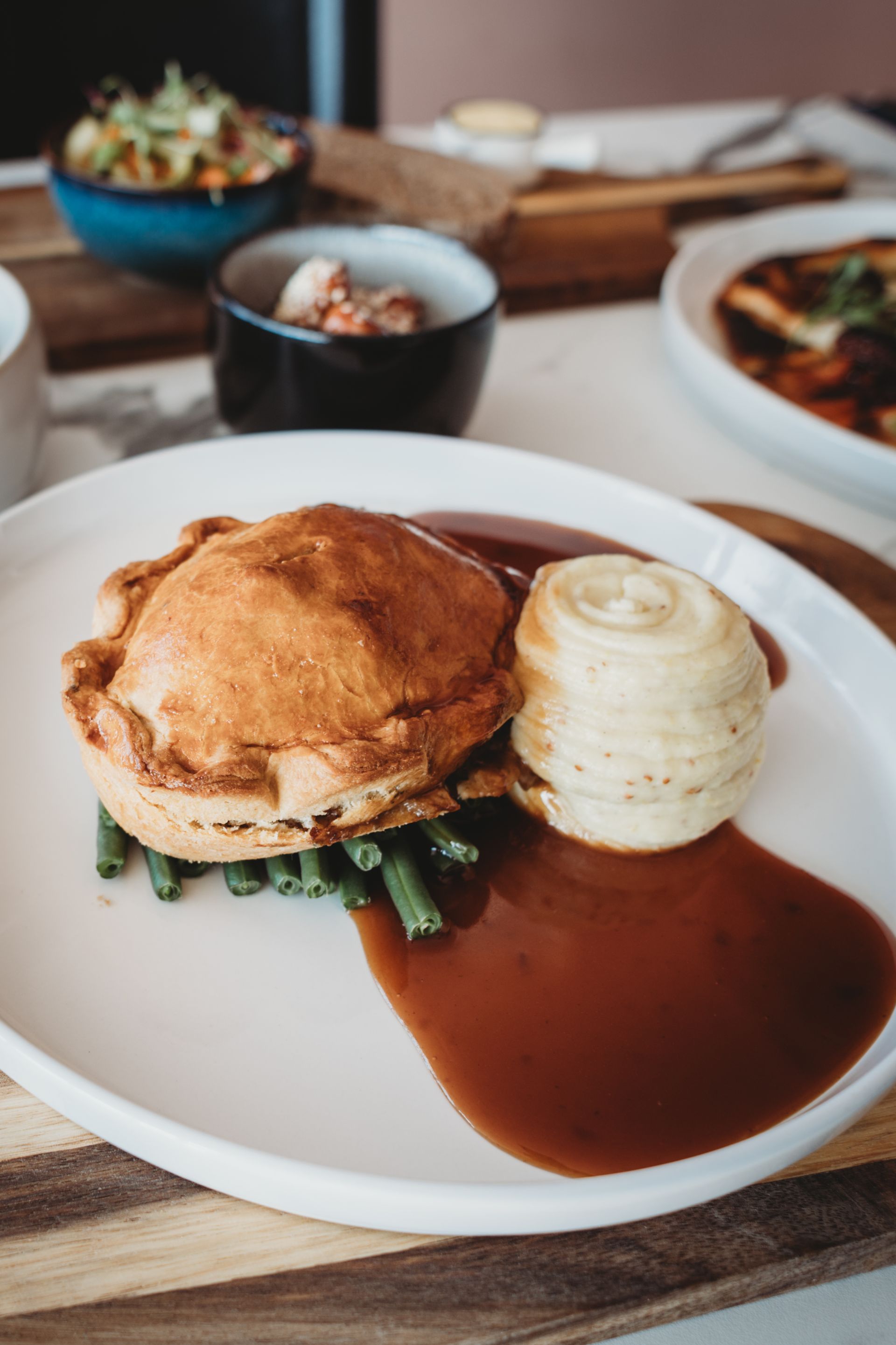 Meat pie with gravy, roasted potato, and green beans on a white plate.