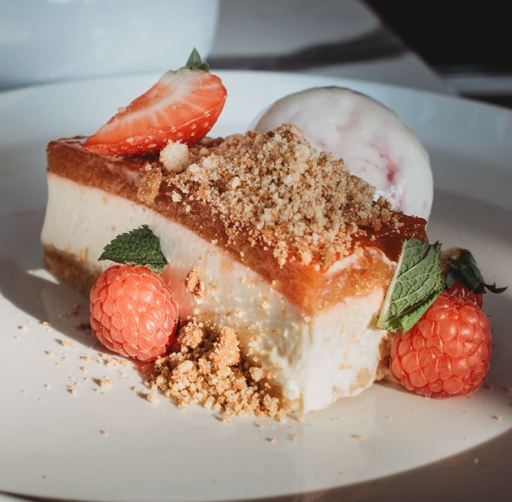 Cheesecake dessert with strawberry, raspberries, crumble, and scoop of ice cream on a white plate.