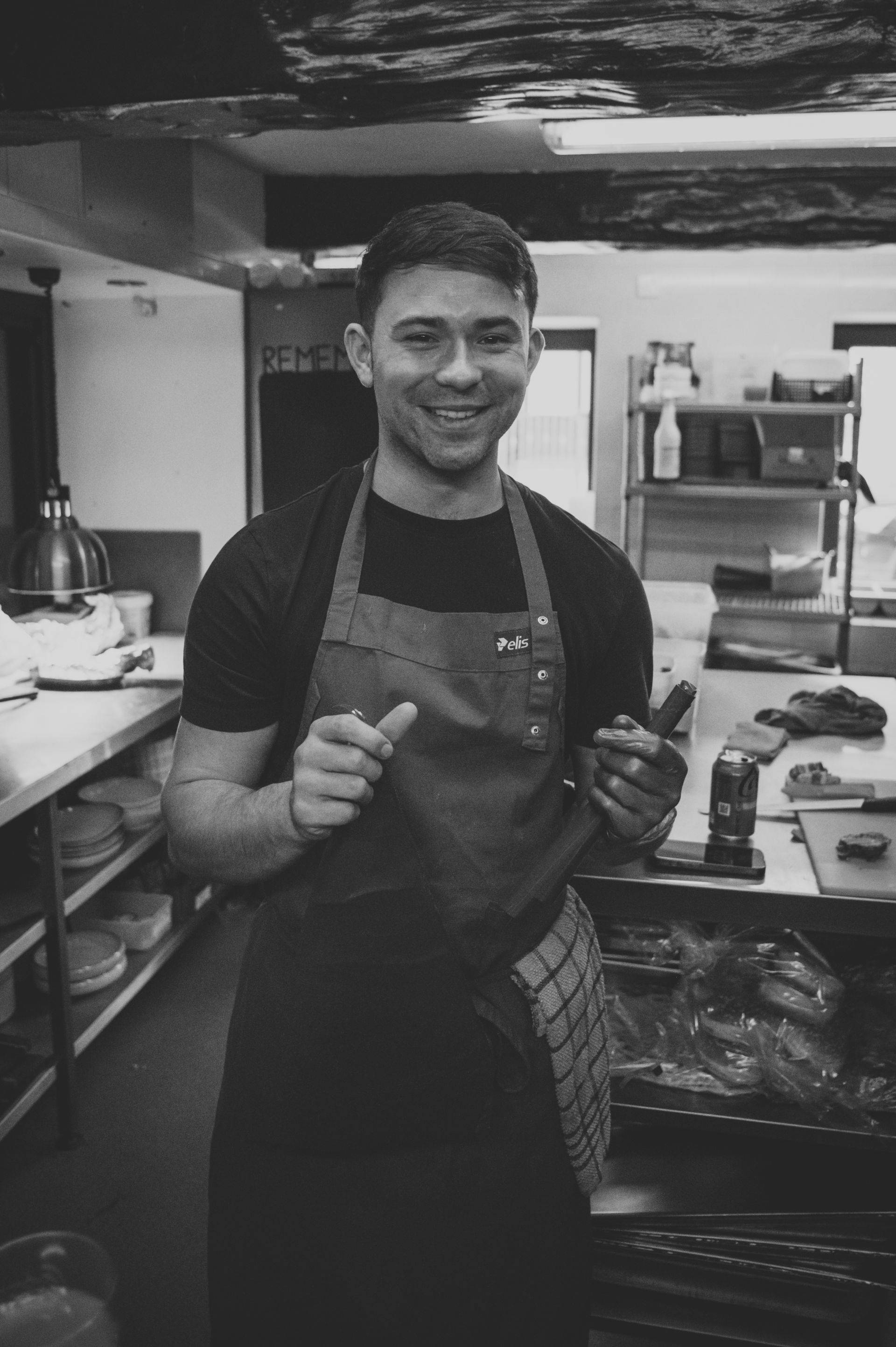 Chef in kitchen, smiling, holding knife, wearing apron.