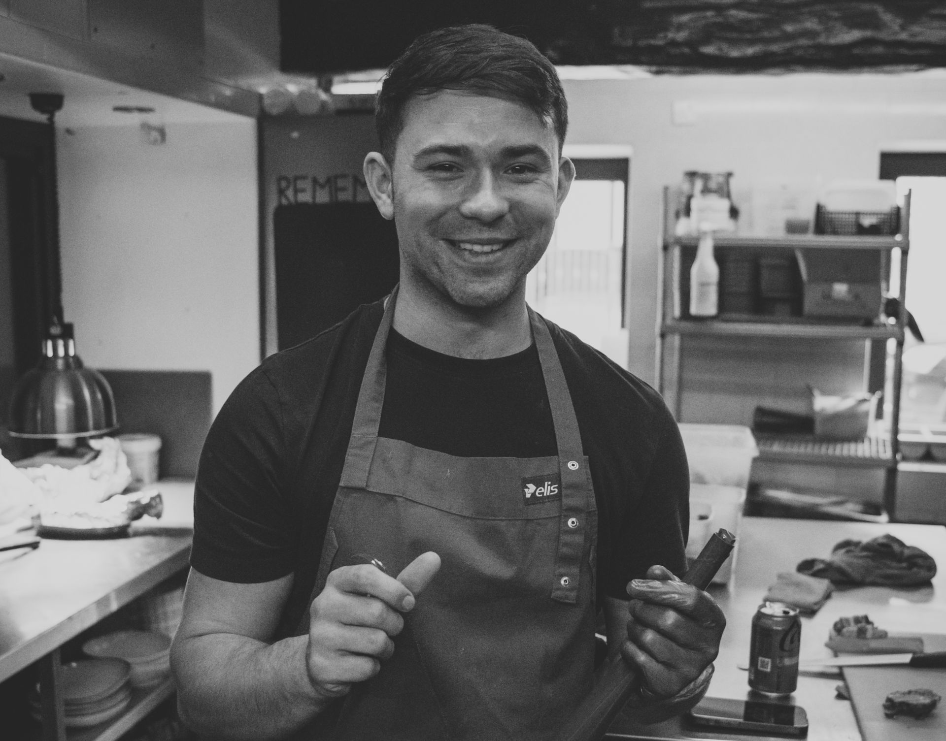 Chef smiling in a kitchen, wearing an apron, gesturing with hands.