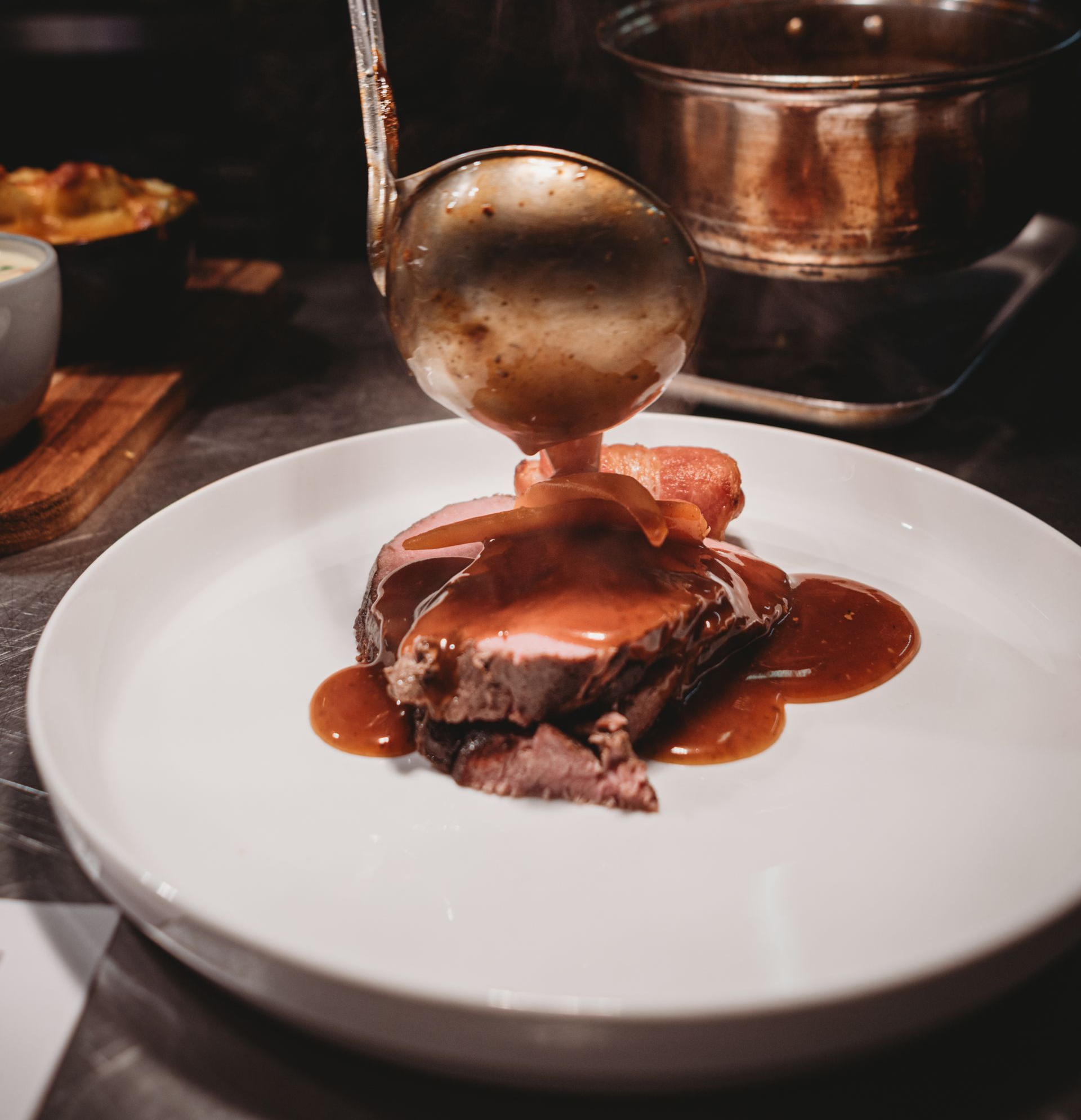 Close-up of a plate with roast beef, potatoes, and gravy being poured from a ladle.