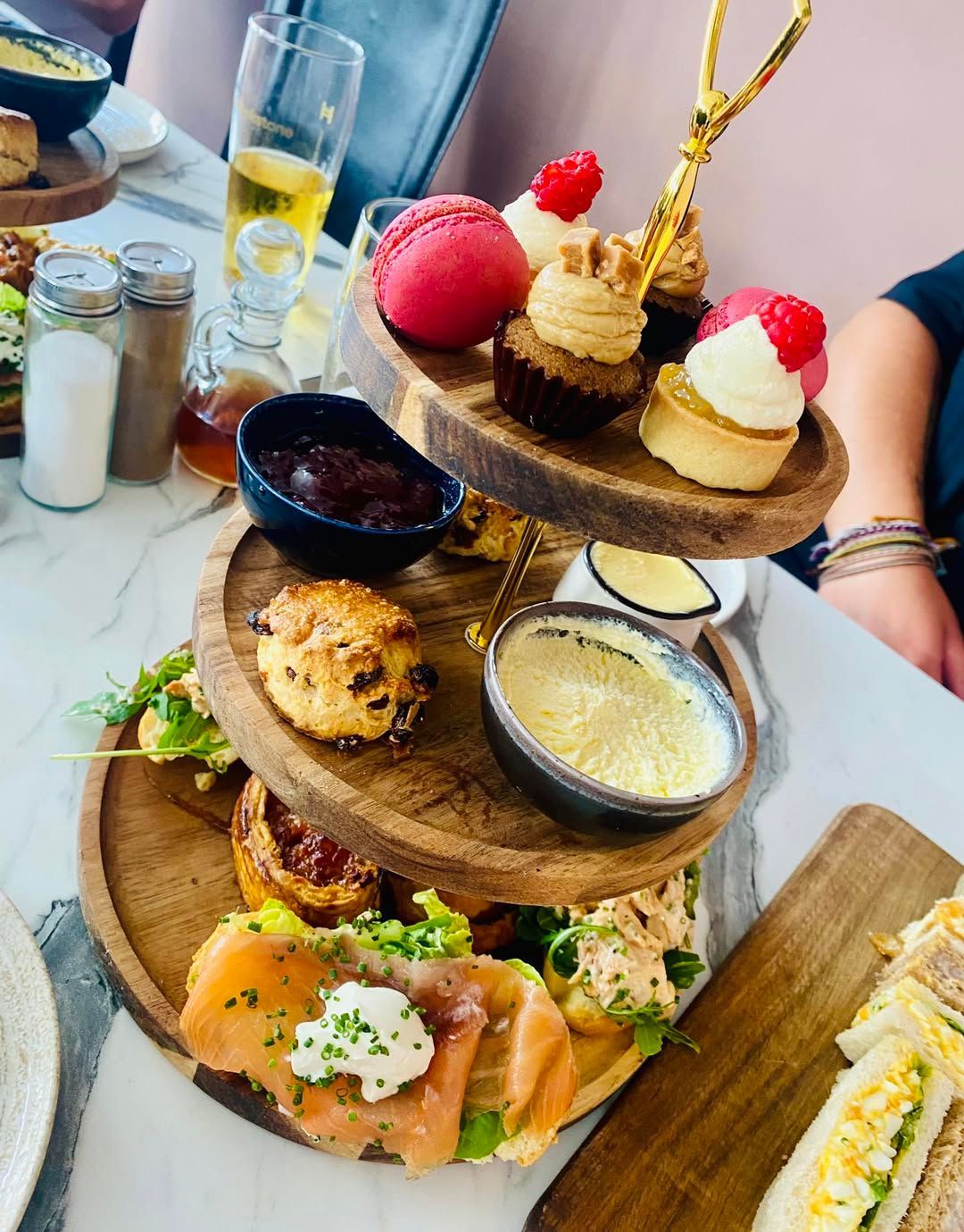 Three-tiered wooden tray of pastries and sandwiches on a table. Afternoon Tea at The Boot & Shoe