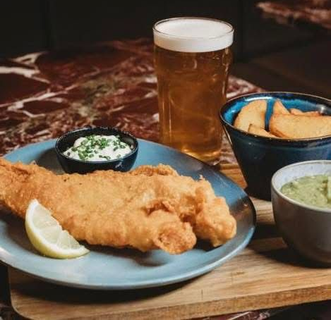 Glass of beer, overflowing with foam on a dark background.