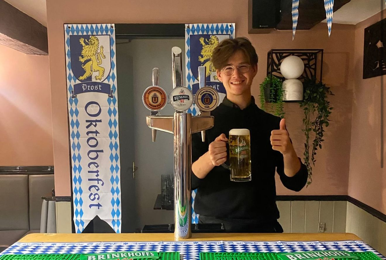 Man behind a bar holding beer, Oktoberfest banner and tap handles visible. at the Boot & Shoe Waterfoot, Rossendale