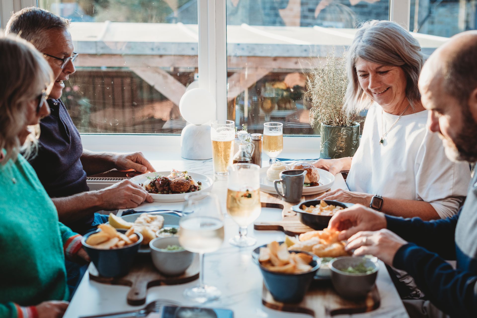 People eating a meal at a table near a window. Includes plates of food and drinks.