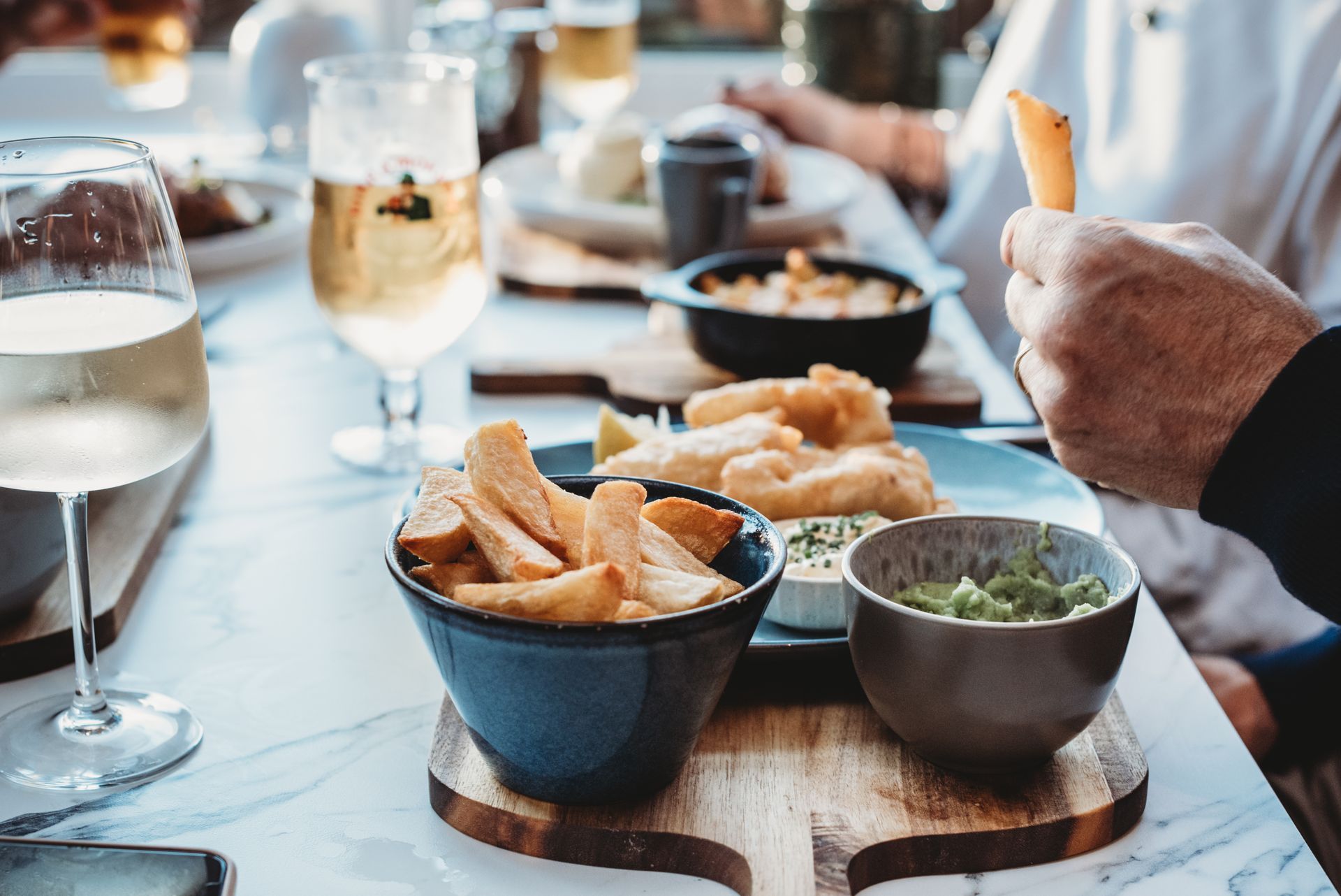 Table with chips, fish, and other dishes; a person holds a chip. Lunch at the Boot & Shoe, Waterfoot, Rossendale