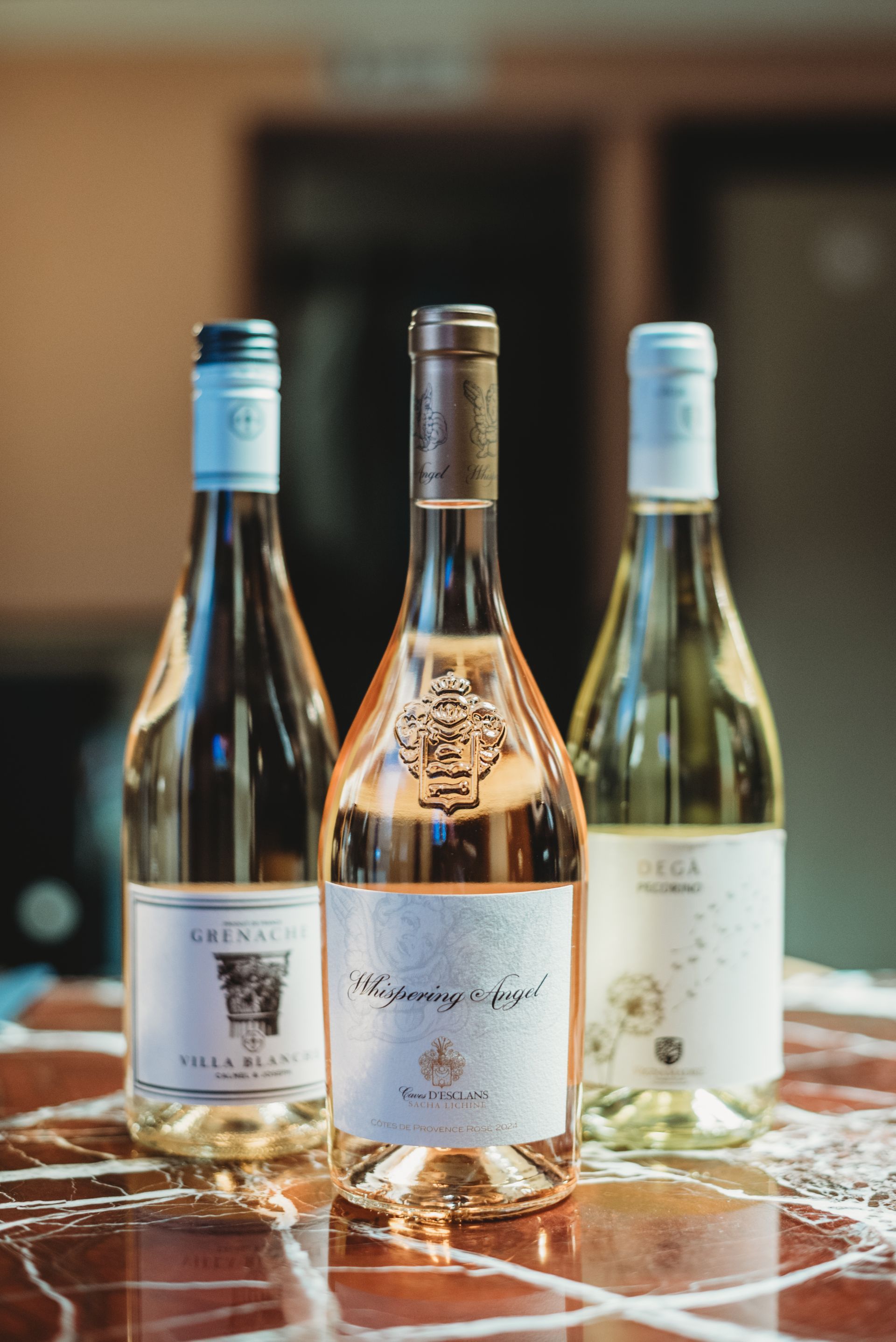 Three wine bottles on a table; one rosé in the middle, two white wines on either side.