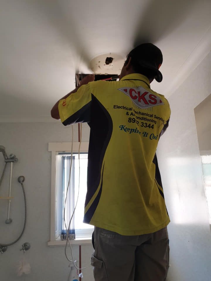 Electrician in yellow shirt working on a ceiling fixture in a bathroom. — CKS Electrical and Air Conditioning in Ciccone, NT