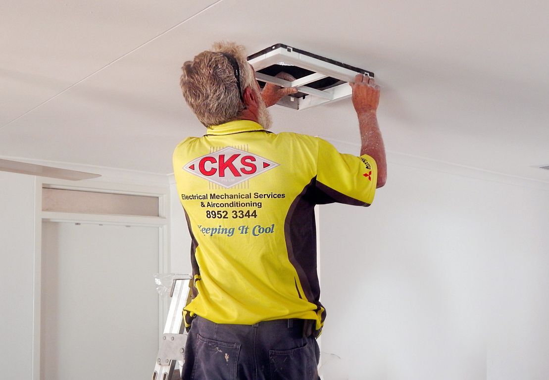 A Person in a Yellow CKS Shirt is Installing a Vent Cover — CKS Electrical and Air Conditioning in Ciccone, NT