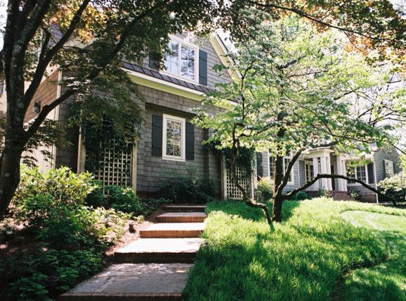 A gray house with a brick path leading to the entrance, framed by trees and greenery.
