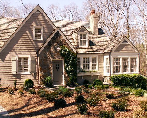 Cottage-style house with stone facade, cedar shake roof, and front yard landscaping.