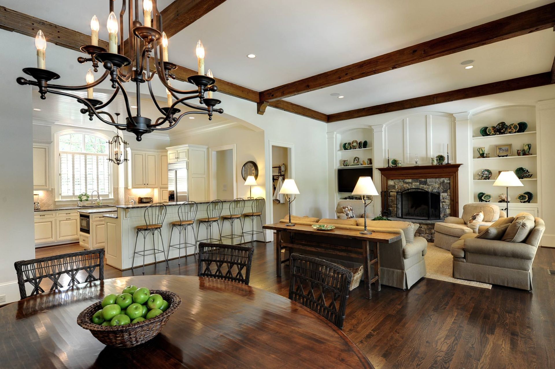 Elegant living room with dining area, kitchen, fireplace, and chandelier.