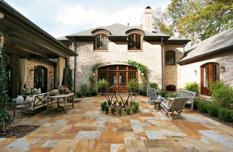 Stone patio with outdoor furniture, surrounding a brick house with arched windows.