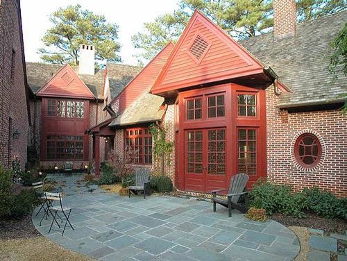 Red brick house with red trim, a stone patio, and two chairs.