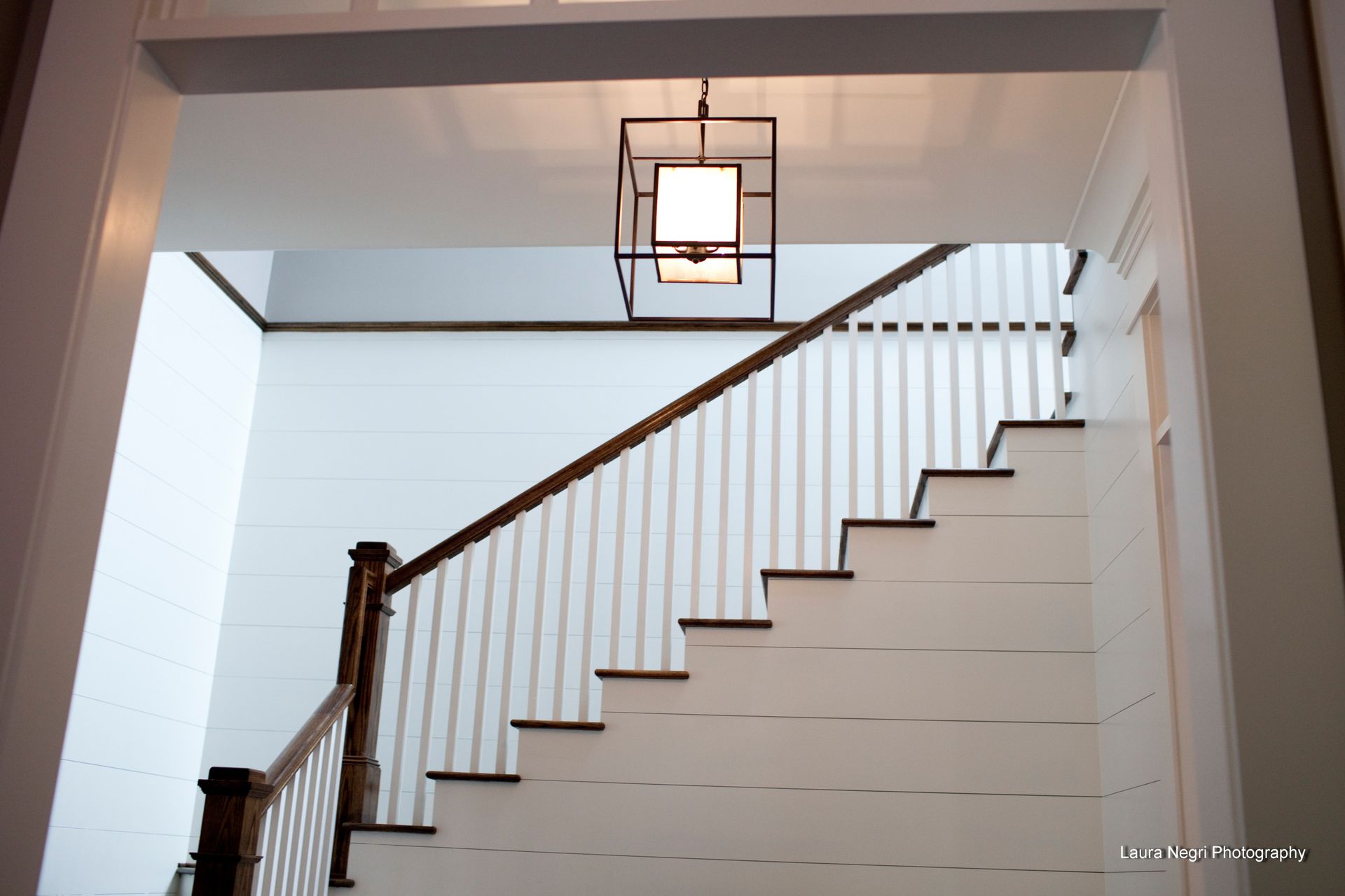 Staircase with white risers, wood handrail, and a hanging black lantern.