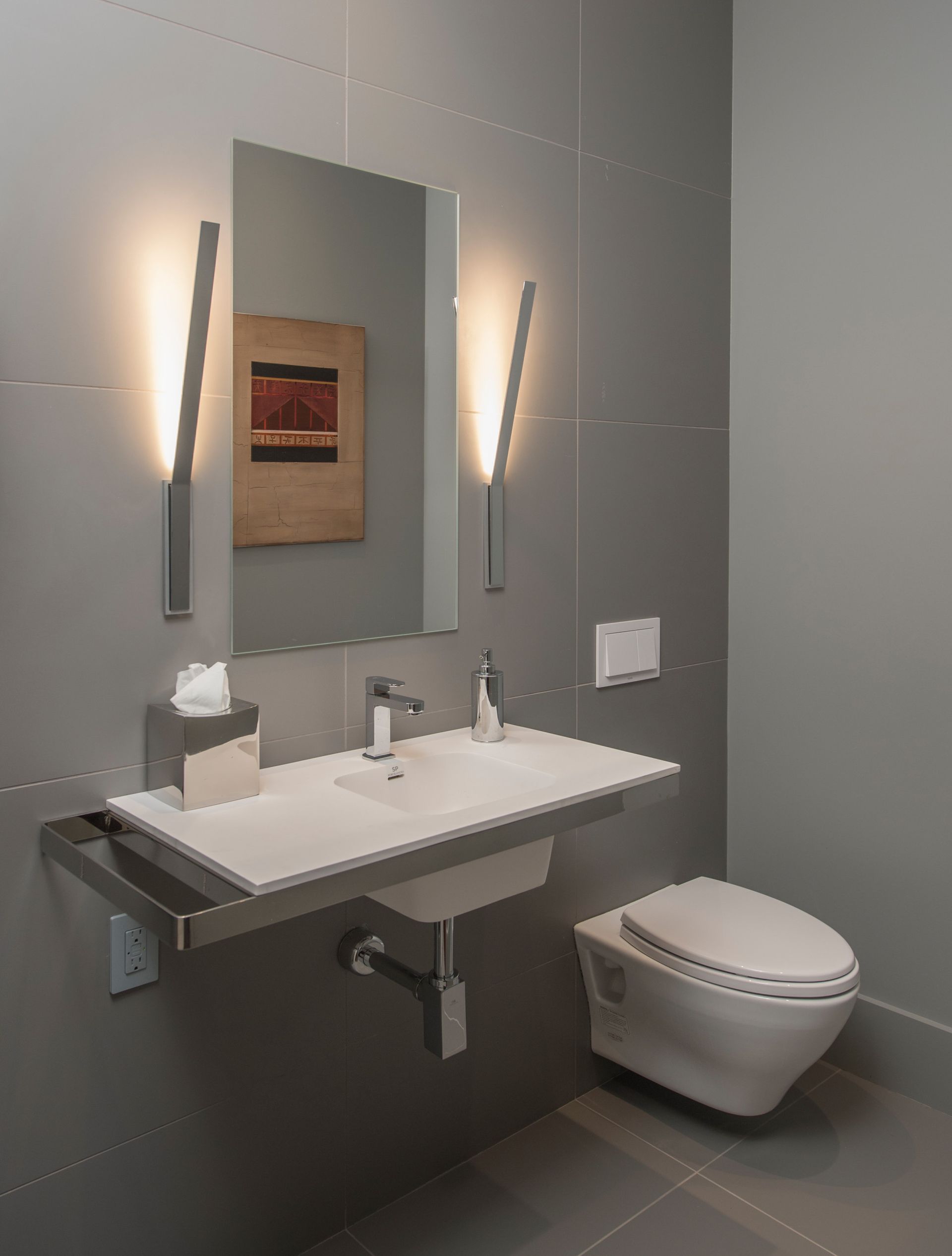Modern, accessible bathroom with wall-mounted sink and toilet, gray walls, and vertical lights flanking a mirror.