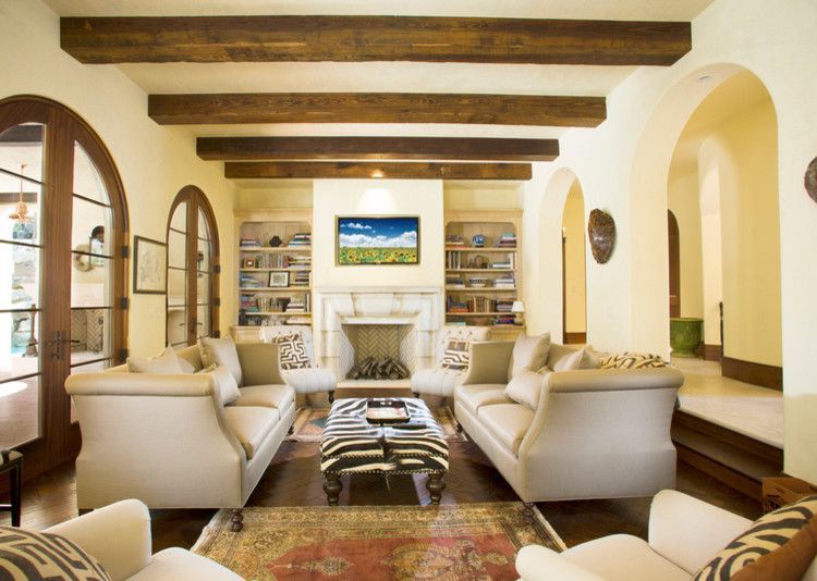 Living room with tan couches, fireplace, wooden beams, arched doorways, and patterned rug.