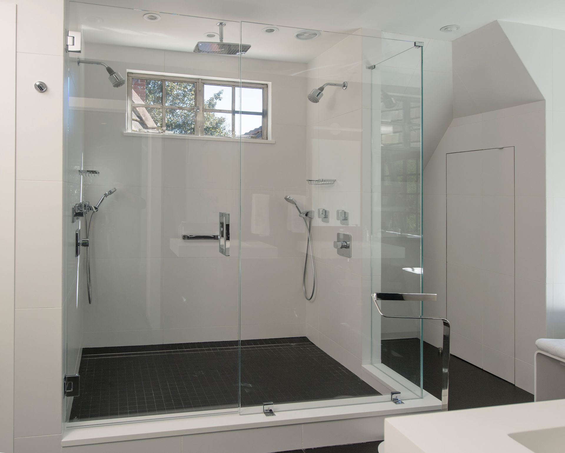 Modern, glass-walled shower with multiple showerheads, black tiled floor, and white walls.