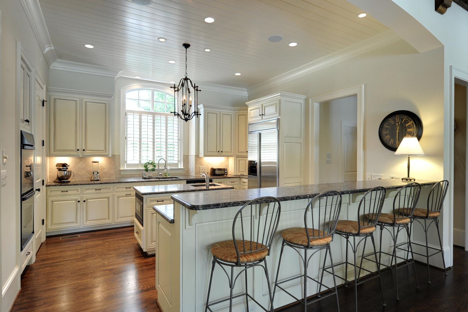 Cream-colored kitchen with island, bar stools, and a view of a room.