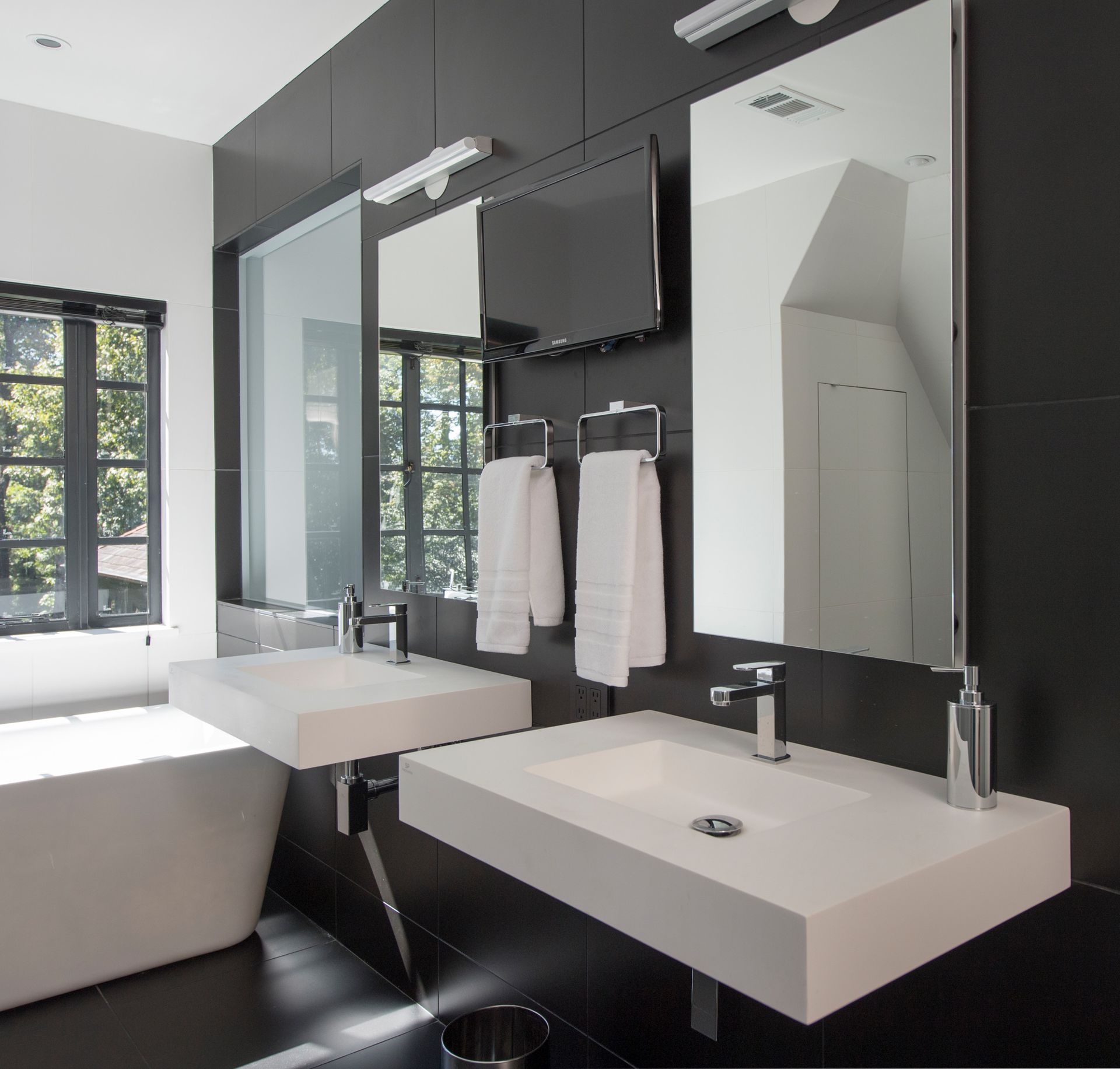 Modern black and white bathroom with two sinks, a TV, and large mirrors.